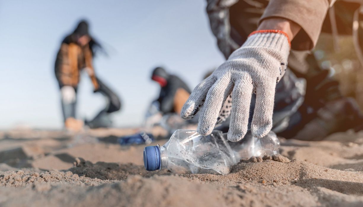 Plastiksammler am am Strand hebt eine leere Flasche auf.