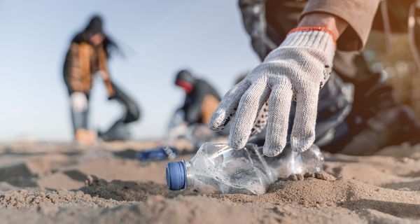 Plastiksammler am am Strand hebt eine leere Flasche auf.