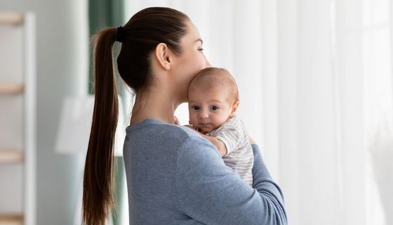 Eine junge Mutter hält Ihr Baby im Arm und schaut in die Ferne.