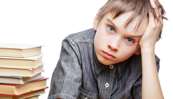 Schuljunge, ca. 9 Jahre alt, greift sich mit trauriger Miene an den Kopf, neben sich einen Stapel Bücher