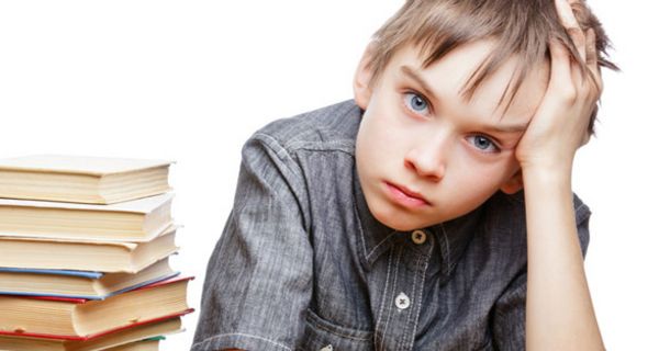 Schuljunge, ca. 9 Jahre alt, greift sich mit trauriger Miene an den Kopf, neben sich einen Stapel Bücher