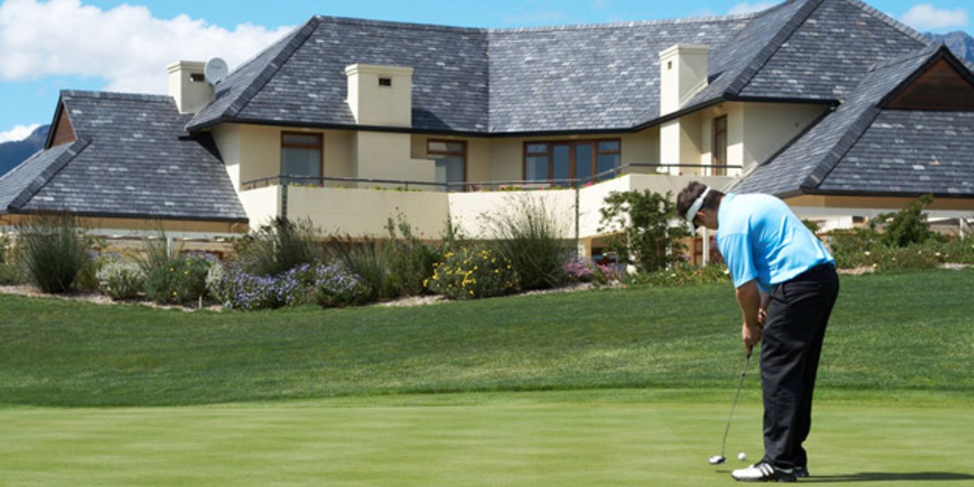 Ein Mann spielt vor einer riesigen Villa Golf auf einem Golfplatz.