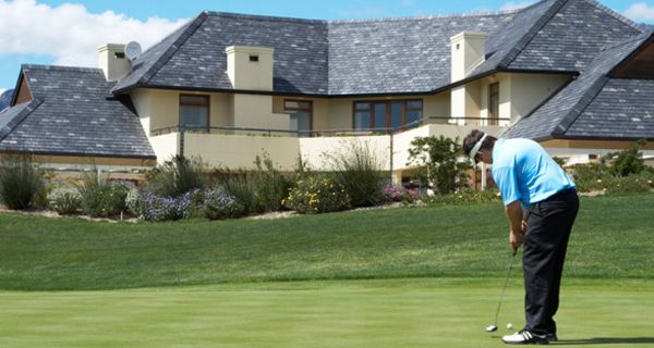 Ein Mann spielt vor einer riesigen Villa Golf auf einem Golfplatz.