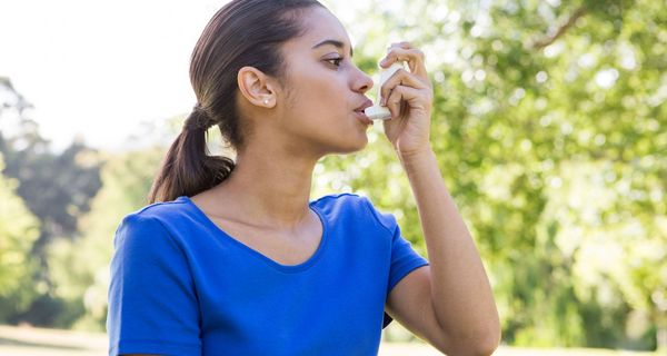 Junge Frau, draußen im Freien, nutzt Asthmaspray.