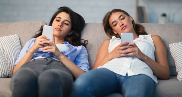 Zwei jugendliche Mädchen, liegen mit ihren Smartphones auf der Couch.