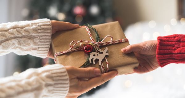 Hände, die ein festliches Geschenk übergeben.