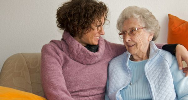 Seniorin sitzt mit Tochter auf dem Sofa.