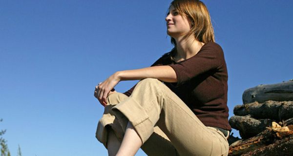 Junge Frau sitzt auf Holzstapel.