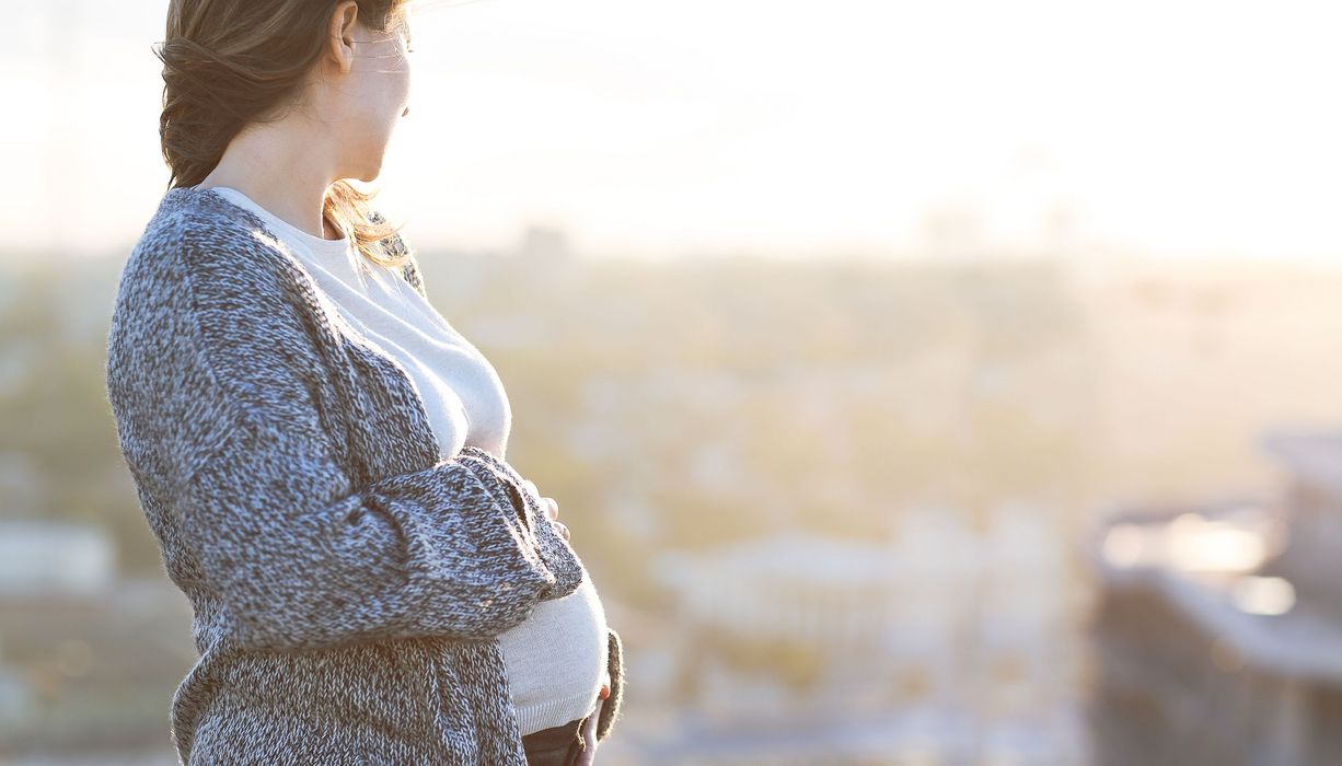 Schwangere Frau, schaut in die Ferne, Stadt-Panorama im Hintergrund.