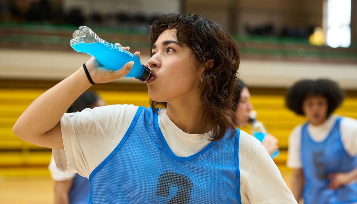Eine jugendliche person trinkt in Sportkleidung einen leuchtend blauen Energydrink.