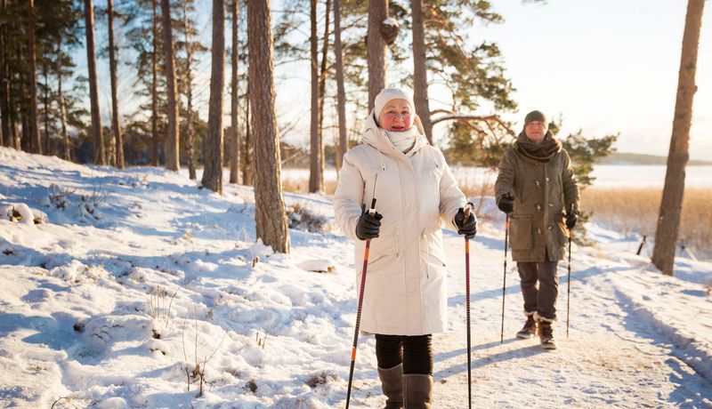 Eine ältere Dame und ein älterer Herr gehen in einem winterlichen Wald spazieren.