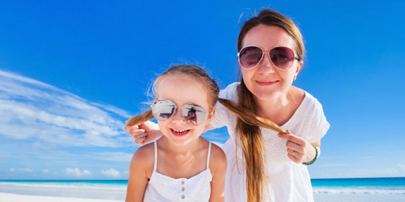 Mutter und 8-jährige Tochter mit Sonnenbrillen am Strand