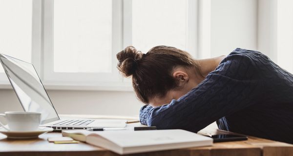 Junge Frau, legt ihren Kopf auf den Schreibtisch.