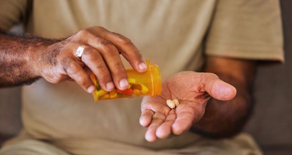 Mann, schüttet sich aus einer Dose Tabletten in eine Hand.