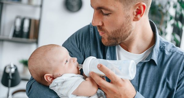 Mann füttert ein junges Baby mit einem Fläschchen voller Muttermilch.
