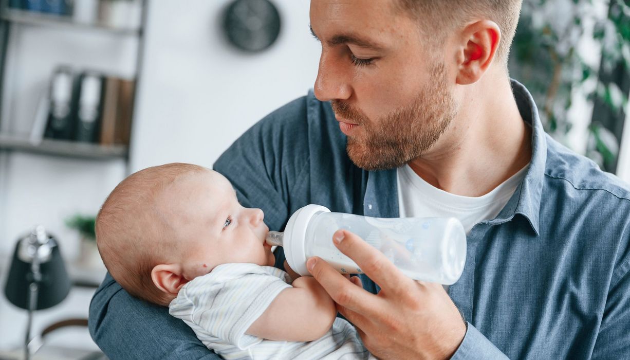 Mann füttert ein junges Baby mit einem Fläschchen voller Muttermilch.