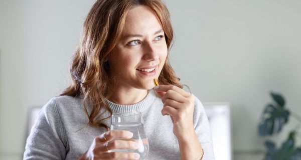 Junge Frau nimmt eine Kapsel, vermutlich Vitamin D, ein.