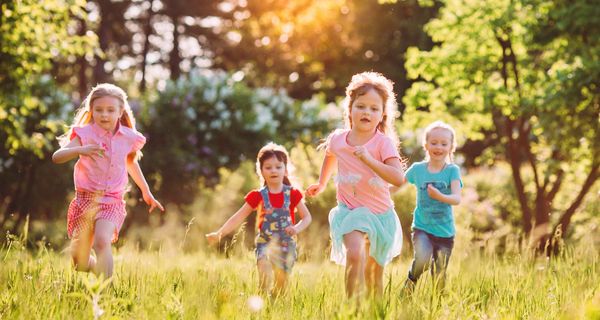 Kinder rennen über eine Wiese mit höherem Gras
