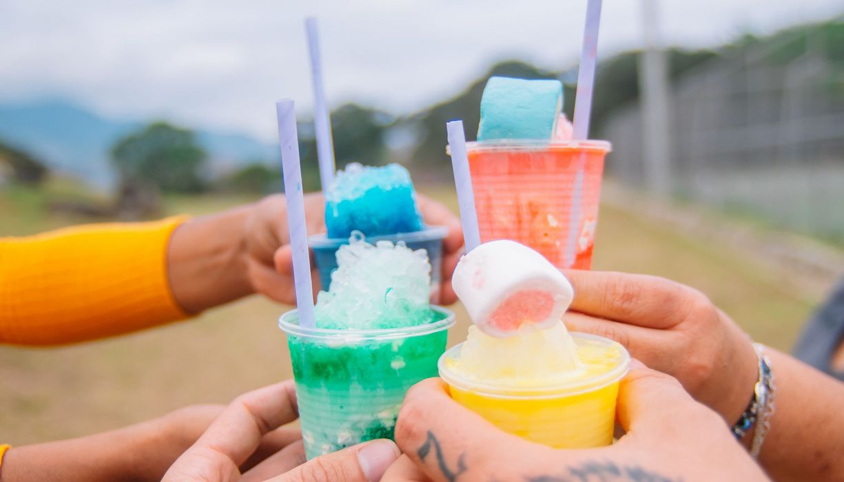 Vier Personen - nur ihre Hände sind zu sehen - stoßen mit bunten Slush-Getränken an. 