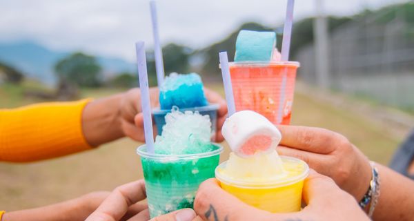 Vier Personen - nur ihre Hände sind zu sehen - stoßen mit bunten Slush-Getränken an. 