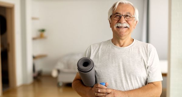 Sportlicher älterer Mann mit Yoga-Matte unter dem Arm.