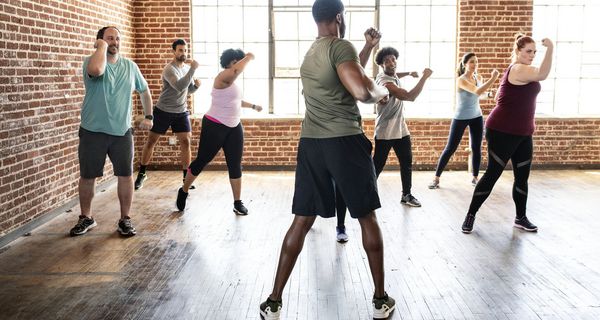 Ein Mann leitet eine Gruppe von Frauen und Männern verschiedenen Alters bei Sportbewegungen an.