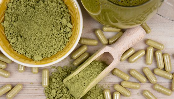 Kratom in Form von Pulver, Kapseln und Getränk auf einem Tisch.