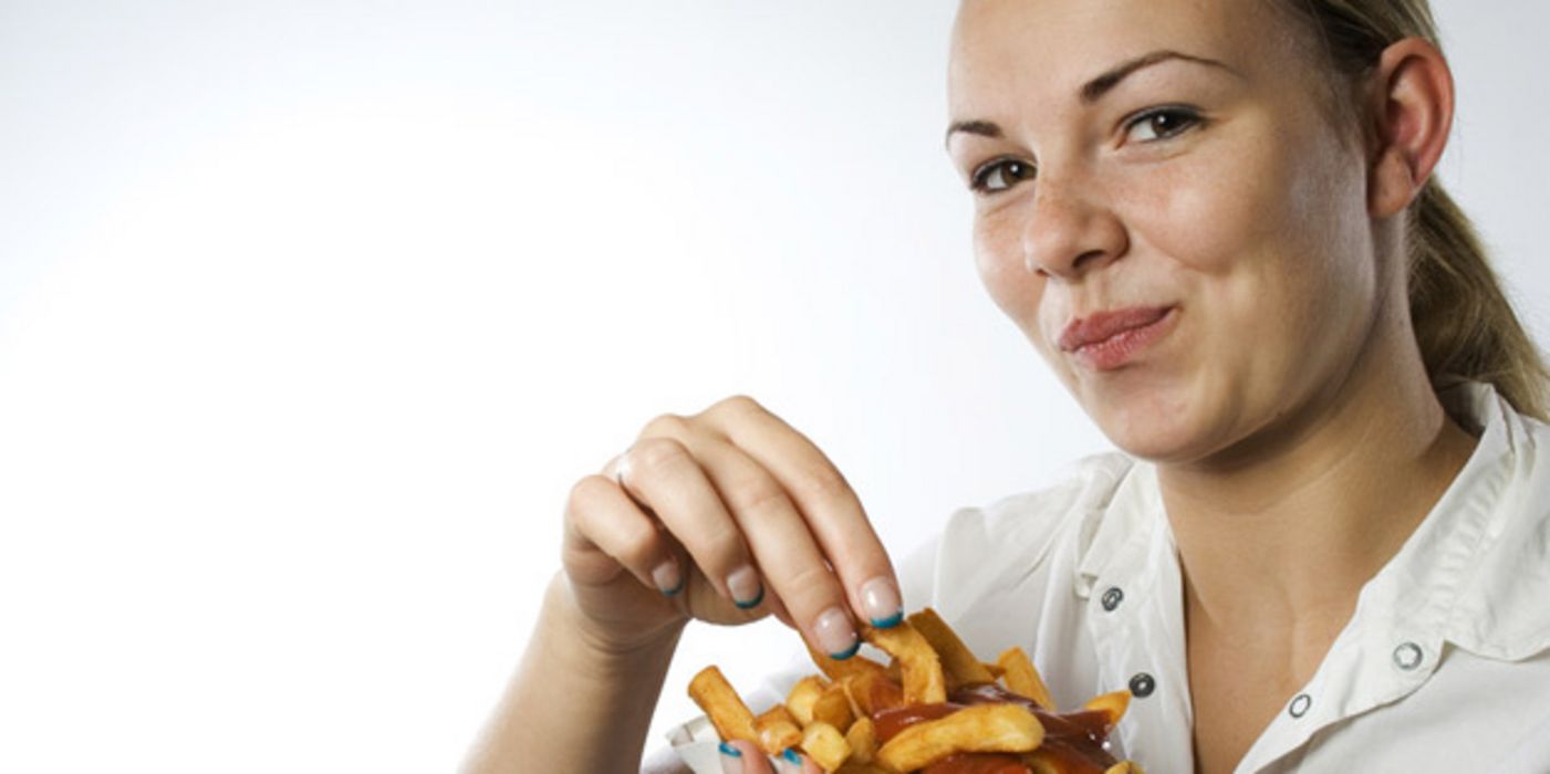 Junge Frau, blonder Pferdeschwanz, beim vergnügten Verspeisen einer Portion Pommes mit Ketchup in Pappschale