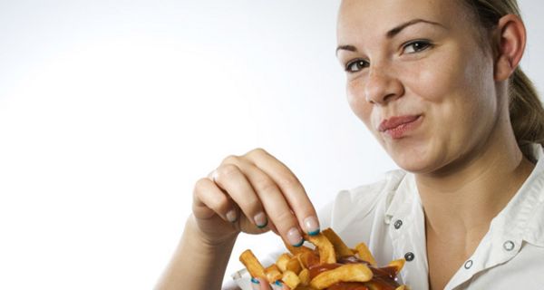 Junge Frau, blonder Pferdeschwanz, beim vergnügten Verspeisen einer Portion Pommes mit Ketchup in Pappschale