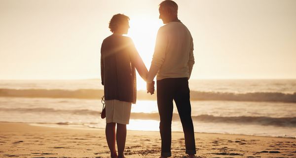 Paar, steht am Strand und hält sich an der Hand.