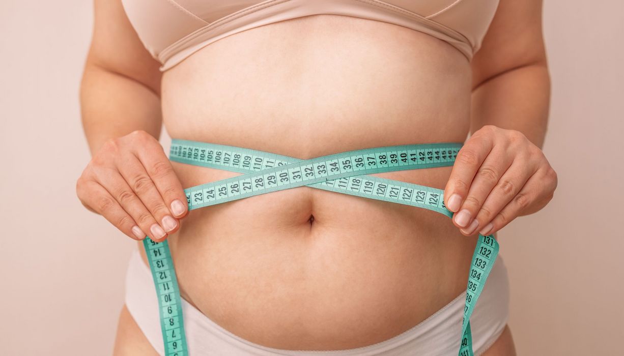 Übergewichtige Frau, hält ein Maßband um ihren Bauch.