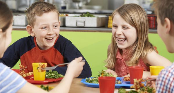 Kinder, etwa 10 Jahre alt, essen in einer Kantine.