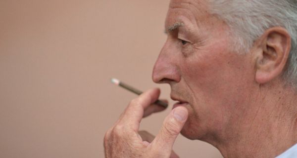 Porträtfoto: Profil Mann um die 70, rechter Bildrand, einen Zigarillo rauchend