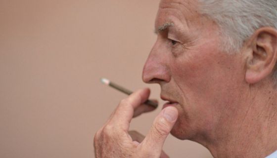 Porträtfoto: Profil Mann um die 70, rechter Bildrand, einen Zigarillo rauchend