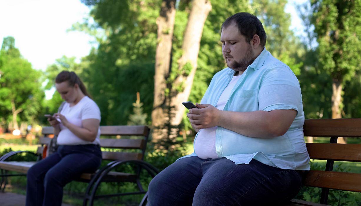 Zwei dicke Menschen, sitzen draußen auf einer Parkbank.