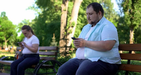 Zwei dicke Menschen, sitzen draußen auf einer Parkbank.