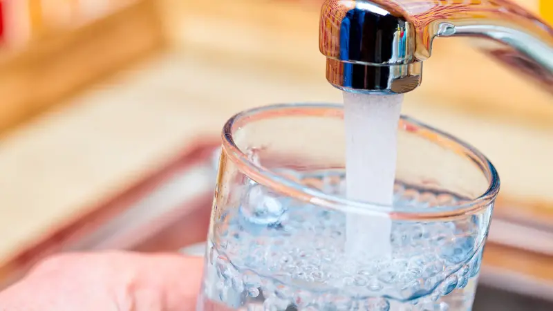 Wasser fließt aus Wasserhahn in ein Glas:
