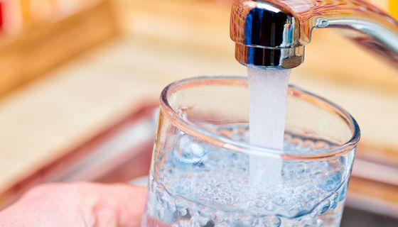 Wasser fließt aus Wasserhahn in ein Glas: