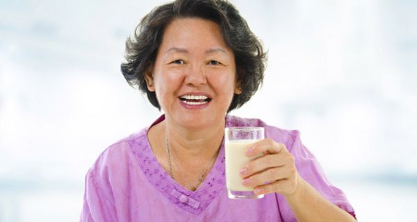 Ältere Asiatin mit einem Glas Milch in der Hand