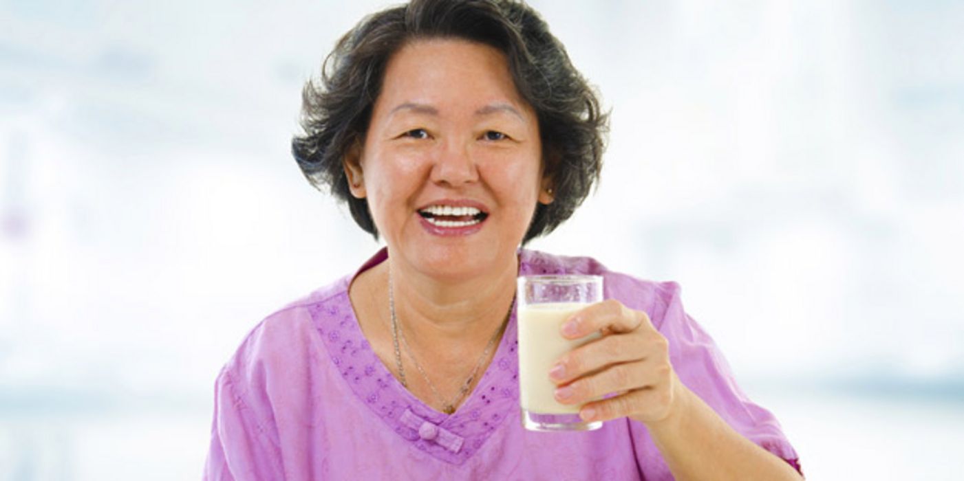 Ältere Asiatin mit einem Glas Milch in der Hand