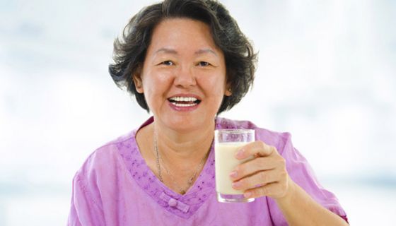 Ältere Asiatin mit einem Glas Milch in der Hand