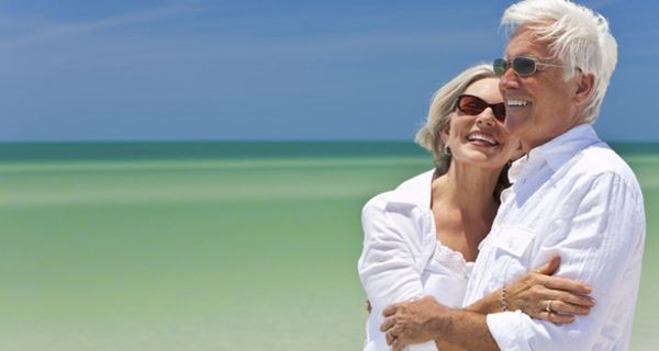 Senioren-Paar in weißer Kleidung am Strand bei gleißendem Sonnenlicht