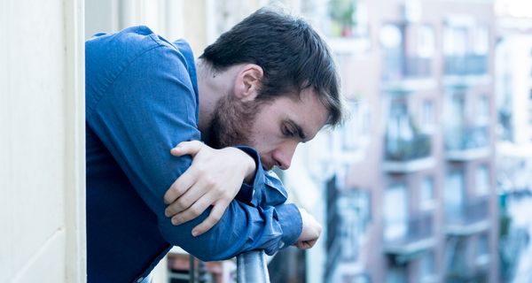 Mann steht am Balkon und schaut deprimiert nach unten