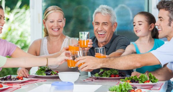 Fröhliche Familie, 3 Generationen, am Esstisch, Salate vor sich, stoßen mit Orangen-Limo an