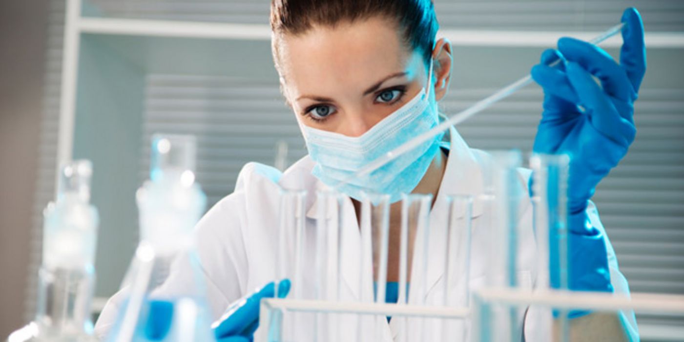 Laborszene: Dunkelhaarige Laborantin, Mundschutz, blaue Schutzhandschuhe, beim Pipettieren