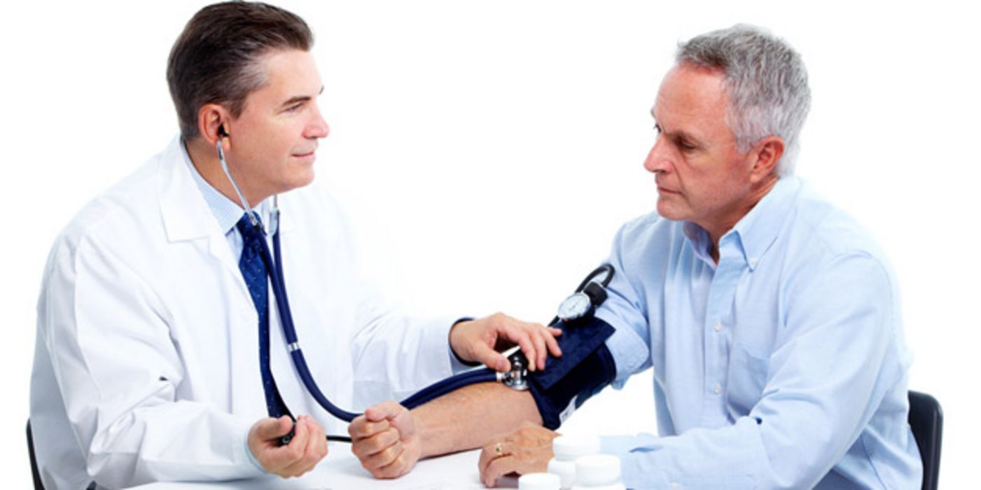 Ein Arzt sitzt einem älteren Patienten gegenüber und misst seinen Blutdruck.