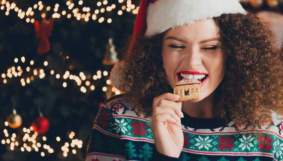 Junge Frau beißt in einen Spekulations-Keks. Hinter ihr ist ein Weihnachtsbaum zu erkennen. Ihre Zähne sind gut zu sehen.
