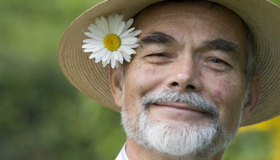 Lächelnder Mann mit Strohhut und Blume hinter dem Ohr.