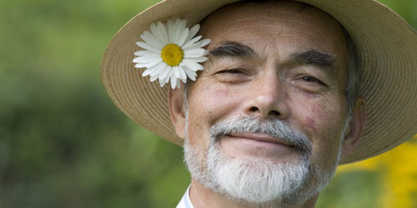 Lächelnder Mann mit Strohhut und Blume hinter dem Ohr.