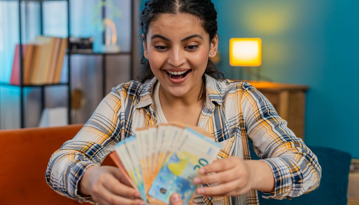 Junge Frau nimmt eine Handvoll 50- und 20-Euroscheine entgegen. Sie freut sich.